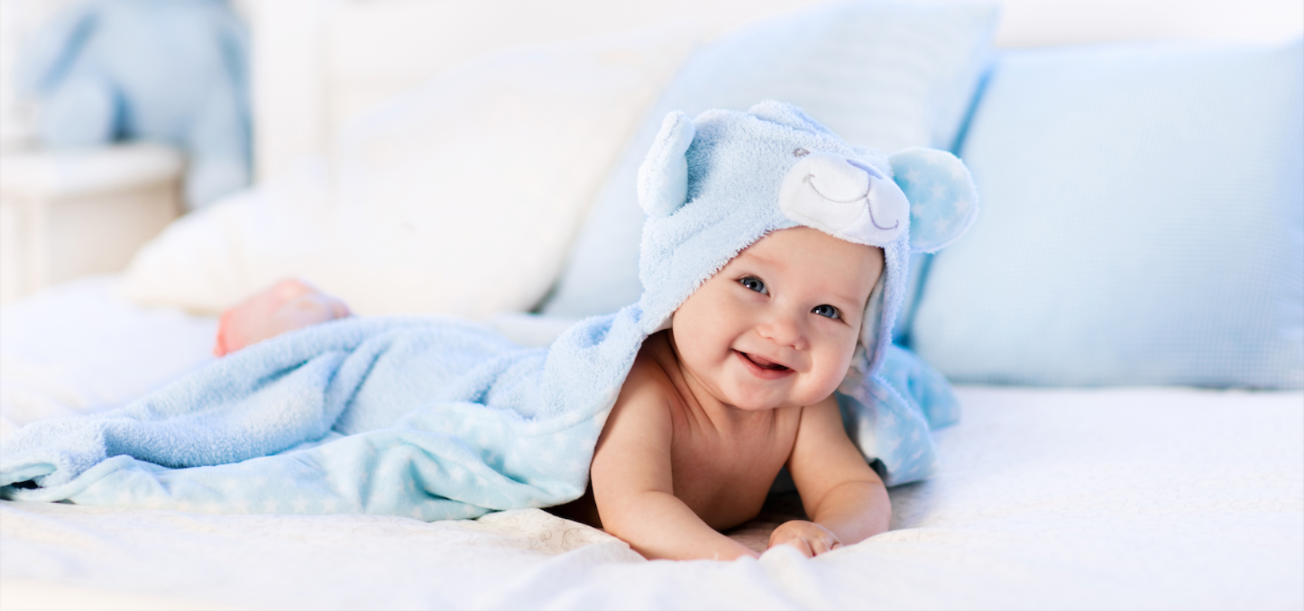 Baby wrapped in a blue towel with a hood, lying on a white surface.